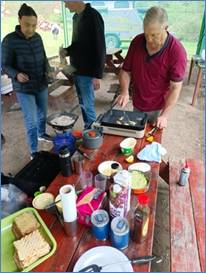 A group of people cooking food on a picnic table

Description automatically generated